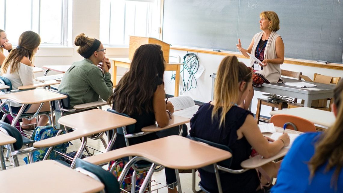 Concurrent Enrollment teacher stands in front of chalkboard teaching to a room of students.