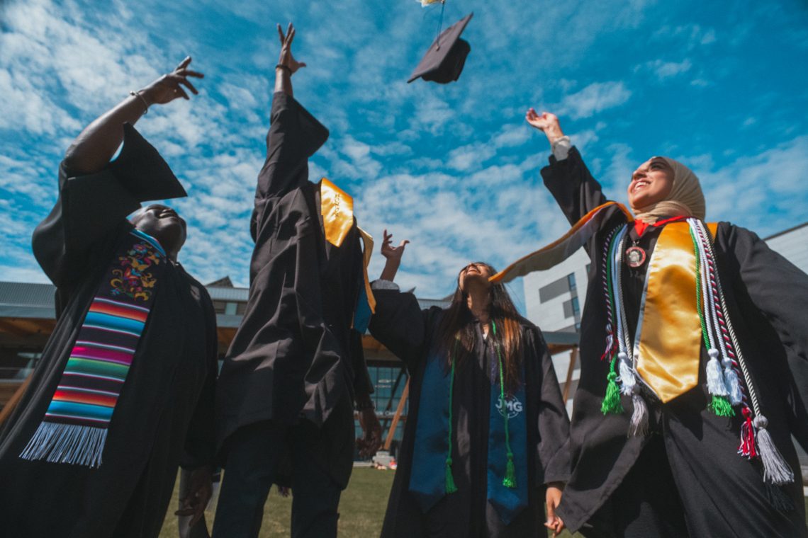 Four students in commencement regalia toss graduation caps in the air.