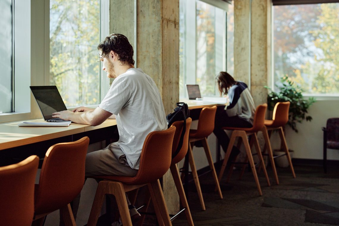 Young man sits at counter, using laptop.