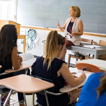Concurrent Enrollment teacher stands in front of chalkboard teaching to a room of students.