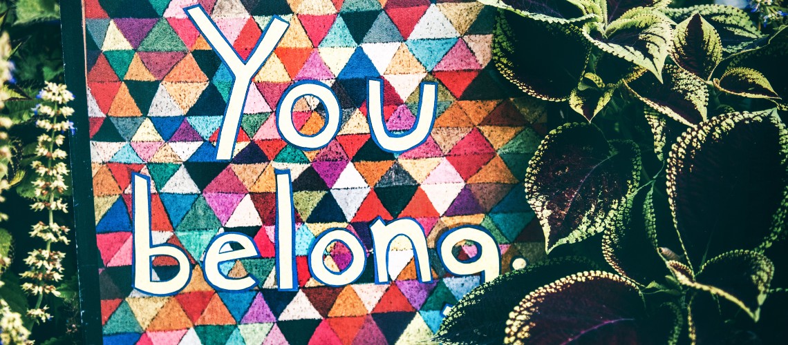 Image by Tim Mossholder. A poster saying "you belong" surrounded by plants.