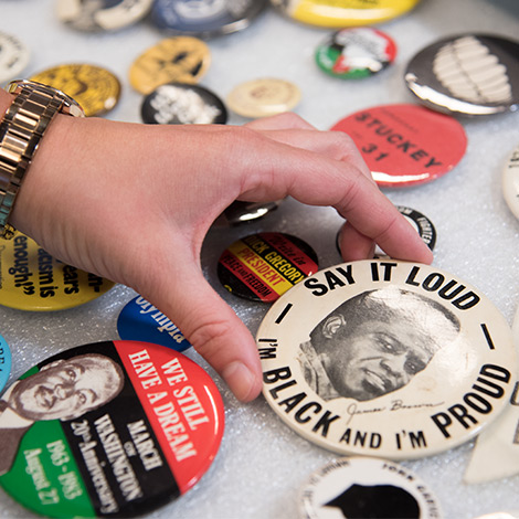 A collection of pins spread on a table, with a hand holding a photo of James Brown and the quote "Say it loud, I'm black and I'm proud."