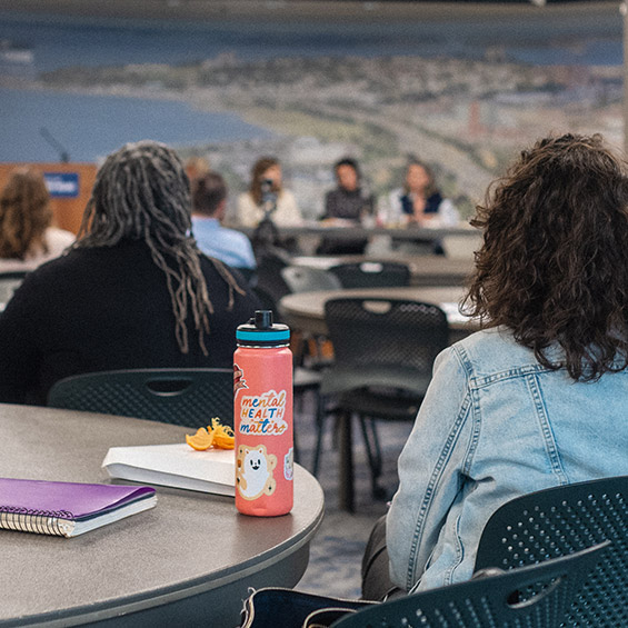 Student sit and listen to a panel discussion, one with a water bottle featuring a sticker stating "mental health matters".