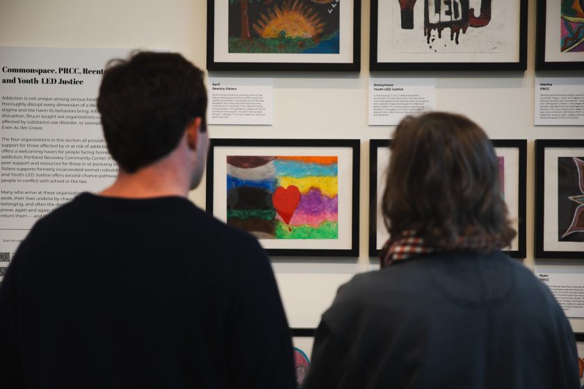 Two people examine a framed pastel drawing of a heart and rainbow, created during a community art workshop as part of USM's 'Even As We Grieve' exhibition at the Crewe Center for the Arts.