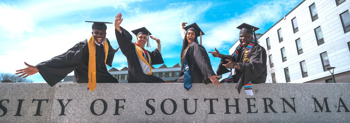 Four USM graduates with caps in the air on USM's Portland campus