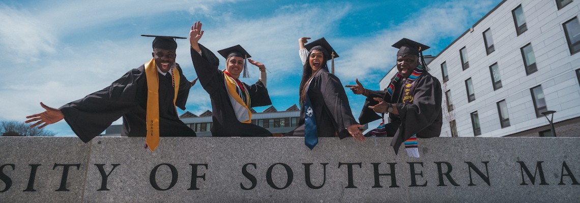 USM grads celebrating on wall in front of McGoldrick center