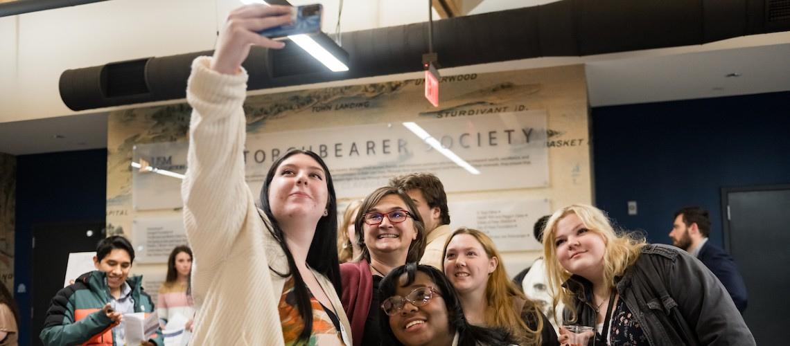 Students taking a selfie in front of Torchbearer Society wall