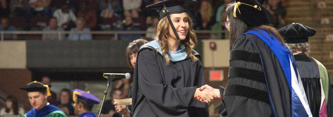 Graduating student shaking hands with President as they accept their diploma