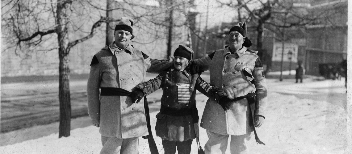 Three men in snowshoe uniforms outside in the snow. Two men are tall, the third is short.