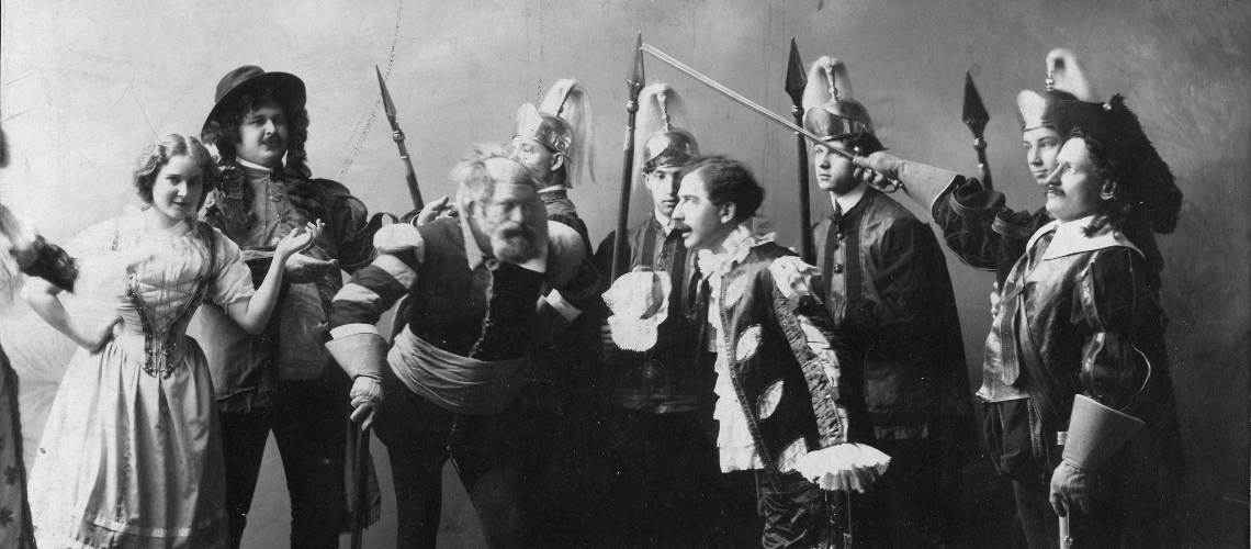 Black and white image of actors in medieval costume posing with prop swords and spears.