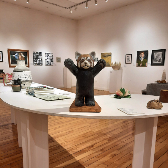 An image of a white curved table with a sculpture of a red panda in the foreground. It is a Gallery and the walls have paintings.