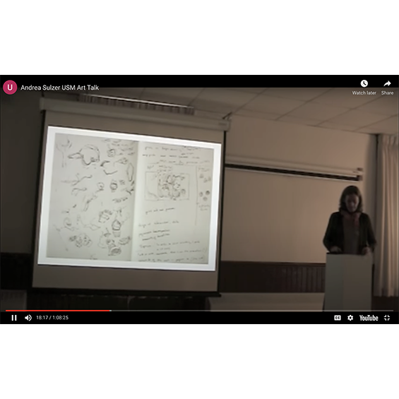 A woman gives a lecture next to a projection of a sketchbook