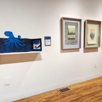 Works by Artist Kate Chenney Chappell. From left to right: "The Octopus," 2011. Artist’s book (pop up accordion: paper, Charbonnel ink, silk cord, collage) 45 in. long x 9 in. wide x10 in. high (open) / 10 x 10 in. (closed). "Mountain Time I," 2011. mixed media (monotype; collage; pine needles) 17 1⁄2 x 24 1⁄2 in.; frame: 26 x 33 1⁄2 in. "Mountain Time IV," 2011. mixed media (monotype; collage with graphite pencil) 15 x 24 in.; frame: 26 x 33 1⁄2 in. "Mountain Time V," 2011. mixed media (monotype; coith; graphite) 17 x 24 in.; frame: 26 x 33 1⁄2 in. Part of "Hidden Stories," Installation view, 2023. University of Southern Maine Art Gallery. Photo by Kat Zagaria Buckley. 