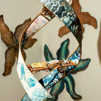 Works by Artist Kate Chenney Chappell. Center front: "Mother Ocean," 2021. Steel rod, printmaking (collagraph/monoprint) on paper, acrylic copper paint) 11 ft. 4 in. x 17 in. wide, on spiral (double helix). "Hidden Stories," 2023. University of Southern Maine Art Gallery. Photo by Tricia Toms. 