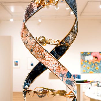 Center front: Kate Chenney Chappell, "Mother Ocean," 2021. Steel rod, printmaking (collagraph/monoprint) on paper, acrylic copper paint) 11 ft. 4 in. x 17 in. wide, on spiral (double helix). "Hidden Stories," 2023. University of Southern Maine Art Gallery. Photo by Kat Zagaria Buckley. 