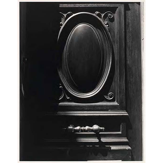 A black and whit ephoto of a door with a circular window in the center. The door seems to be made of wood and is ornate.