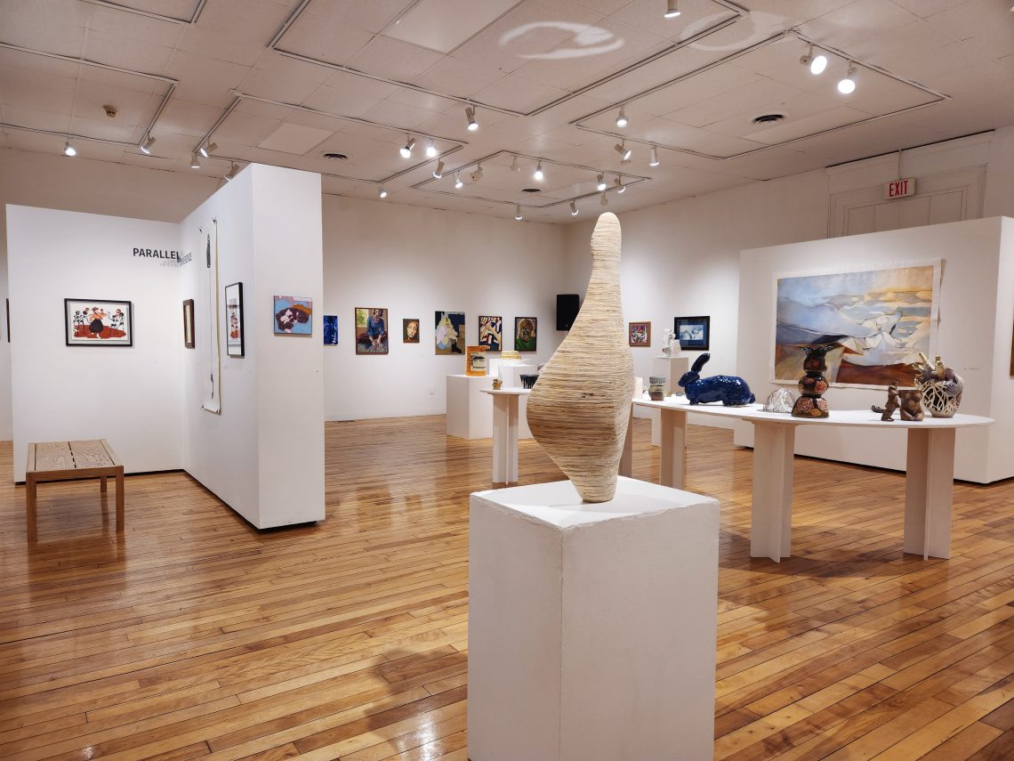Installation view, "Parallel Convergence: The 2023 University of Southern Maine Juried Student Exhibition," University of Southern Maine Art Gallery. Foreground: Molly Rea, "Fixation," 2022. Plywood. 15 in. wide x 33 ½ in. tall x 16 in. deep. 2nd Place Winner, Best-in-Show.