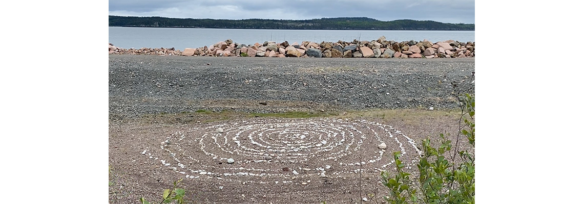 A spiral of stones on a beach with wter and mountains visible in the background