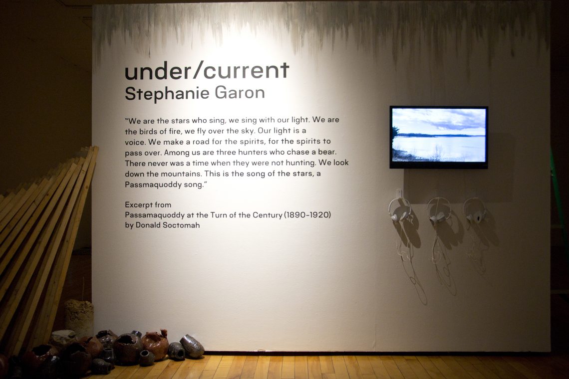 Stephanie Garon, "under/current," 2024. Installation, dimensions variable. Right side; Stephanie Garon, "Scattered Trees of a Storm-Swept Plain," 2024. Single channel video, running time 8 min 24 sec. Audio features Lucy Lippard, writer, activist, curator; Dwayne Tomah, Director of the Wabanaki Museum and Historic Preservationist of the Passamaquoddy Tribe; Severine Von Tscharner Fleming Welcome, Founder and Director of Smithereen Farms; Margaret Struzik, Pembroke Town Clerk; Mali Obomsawin, Musical artist; basket by: Passamaquoddy weaver Deborah Brooks of Sweet Grass Basketry. Filmed at Sipiyak/Pleasant Point and Indian Reservation, Maine, Potomac River. Installation view,"under/current" exhibition, University of Southern Maine Art Gallery, 2024. Photo: John Harlow.