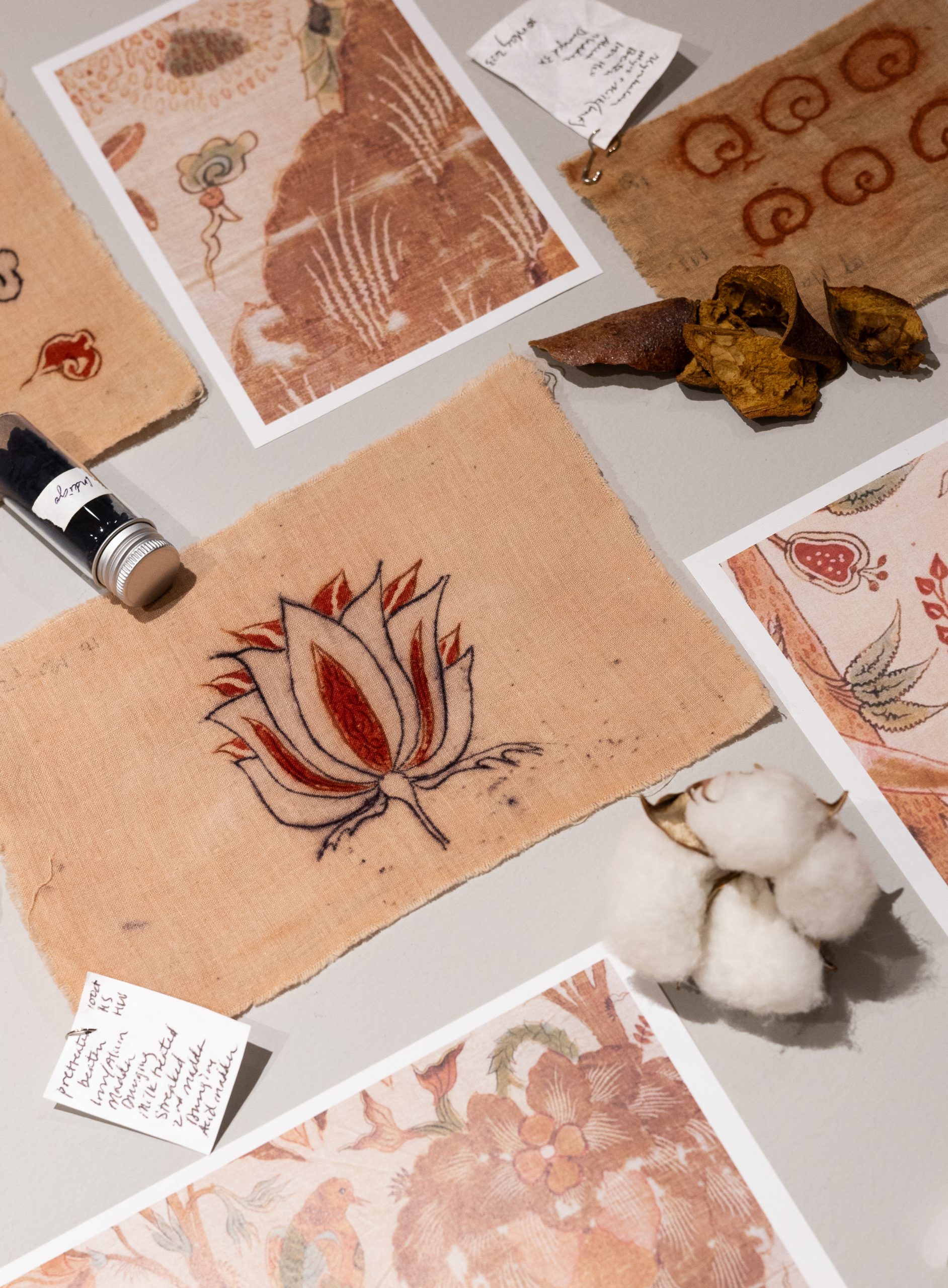 Elaine K. Ng, "Process table" (detail) 2025. Cotton bolls, cotton flower sepals, raw cotton fiber, empty cotton boll, cotton seeds, bamboo styluses, wooden styluses, ground madder root in container, rusty nails in container, indigo chips in container, dyed madder cloth samples, pomegranate rinds, myrobalan pods, paper prints of chintz details; dimensions variable. Photo: Marion Earley.