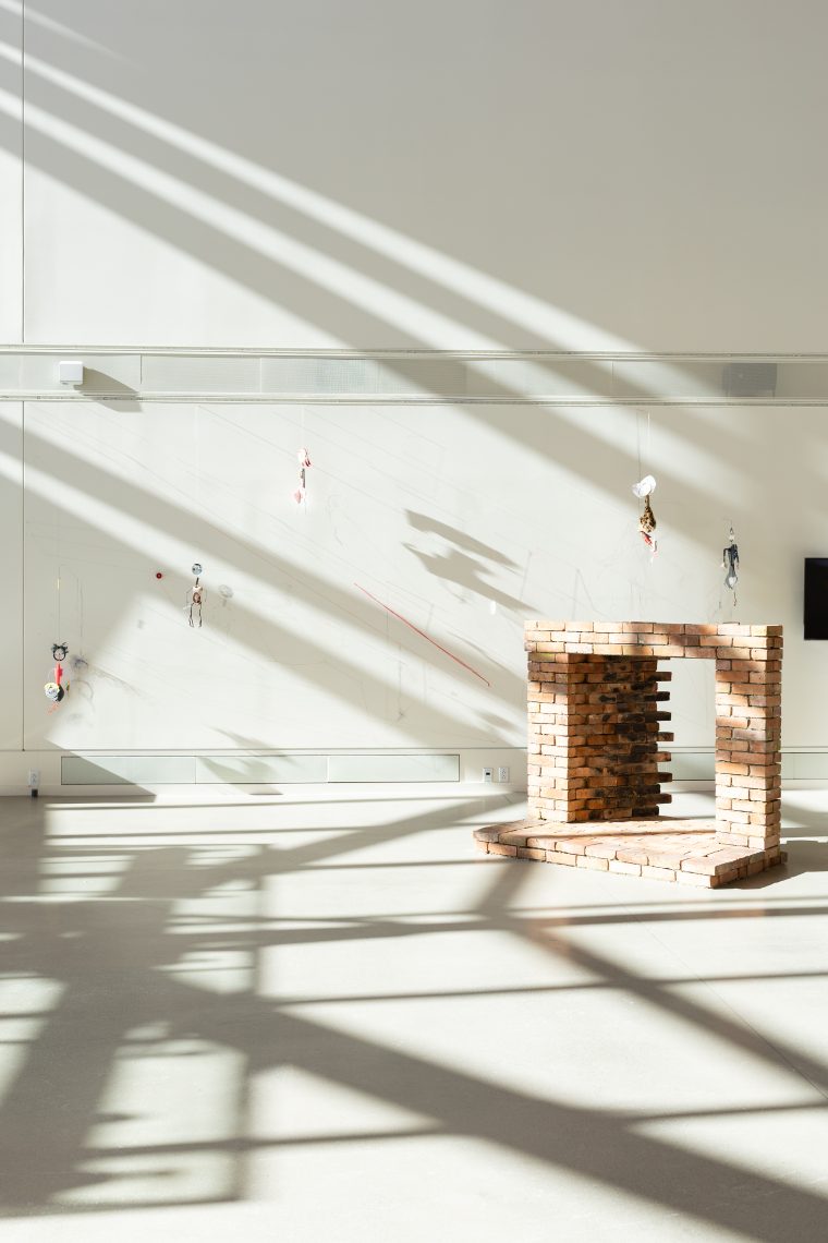 Work by artist Kristin Mariani. Right: "Hearth II," 2026. 150 yr old chimney brick and hearth tile from Maine, local clay mortar; 54 in. high x 64 in. wide x 55 in. deep. Brick structure made in collaboration with Ken Hoffmann. Part of "Of Sibyls and Source: Ranges and Ruptures," 2026. Crewe Center for the Arts at the University of Southern Maine. Photo: Marion Earley.