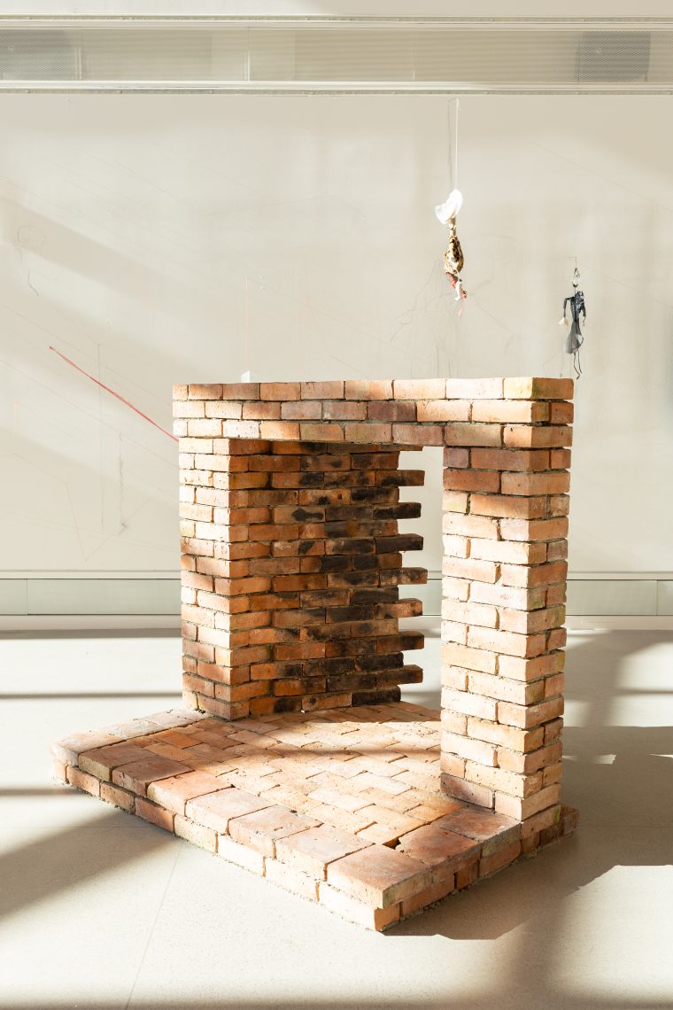 Foreground: Kristin Mariani, "Hearth II," 2026. 150 yr old chimney brick and hearth tile from Maine, local clay mortar; 54 in. high x 64 in. wide x 55 in. deep. Brick structure made in collaboration with Ken Hoffmann. Part of "Of Sibyls and Source: Ranges and Ruptures," 2026. Crewe Center for the Arts at the University of Southern Maine. Photo: Marion Earley.