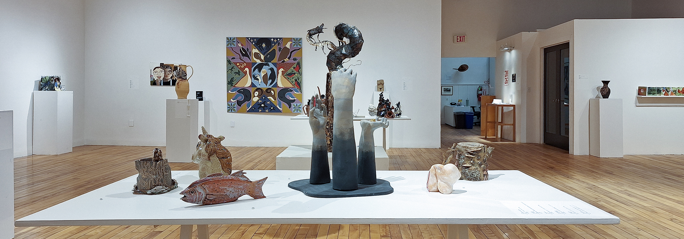 A wide view of a gallery featuring a white table in the foreground with many ceramic objects.