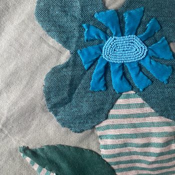 An image of an appliquéd work featuring a flower. Different blue fabrics with patterns create its outline.
