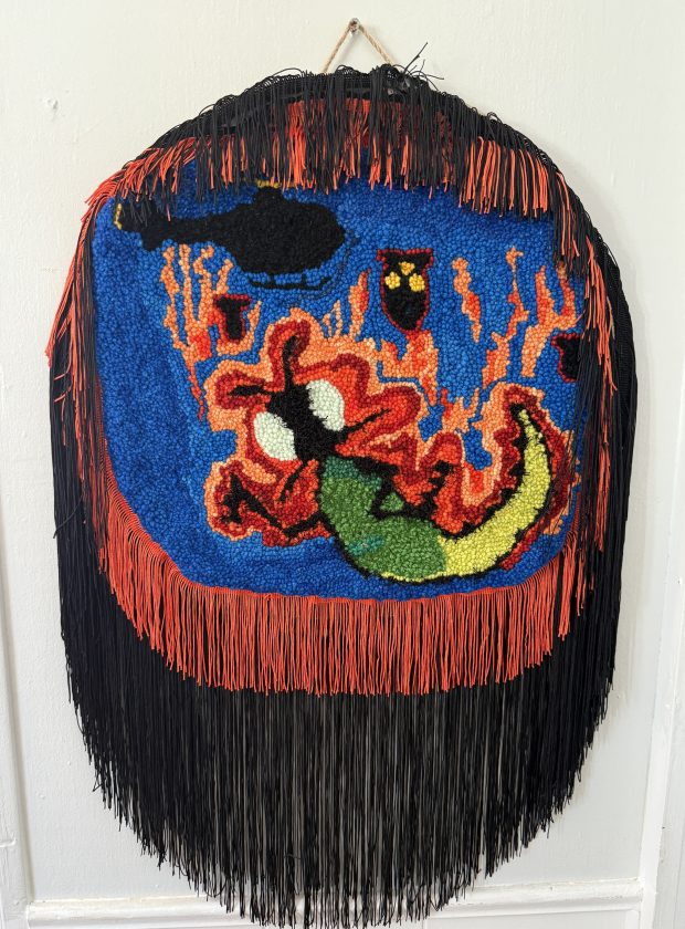 An embroidered piece with black and red fringhe showing caterpillary creatures at the center.