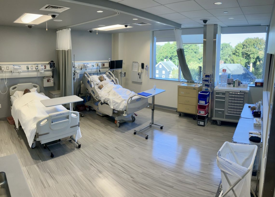 A simulation hospital space containing two beds, each with a mannequin in it. A curtain to separate the beds is drawn back. Many pieces of medical equipment, including monitors sit between and behind the beds. On the ceiling, five observation cameras and two microphones can be seen.