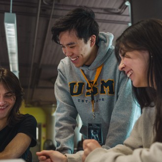 Three students smiling, sitting at a tabling studying