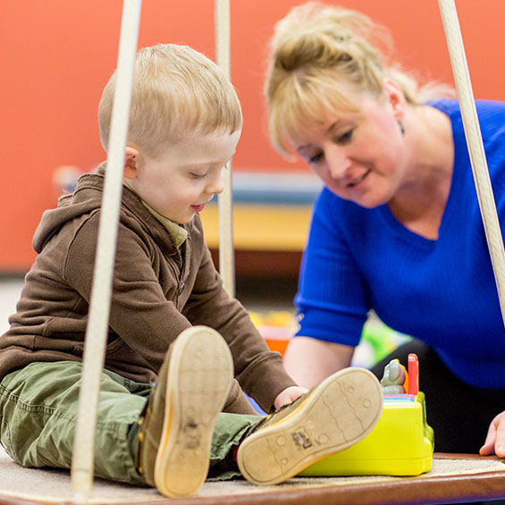 A student works with a child who is seated on a platform swing in our occupational therapy clinic.