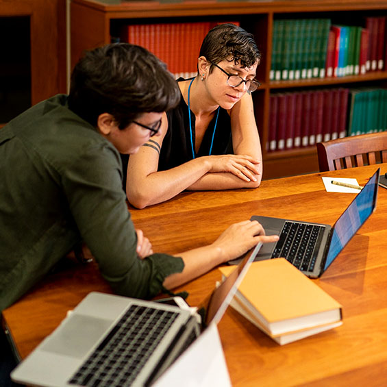Two students work together at a table in our Glickman library. There are two open laptops on the table and a small stack of books.