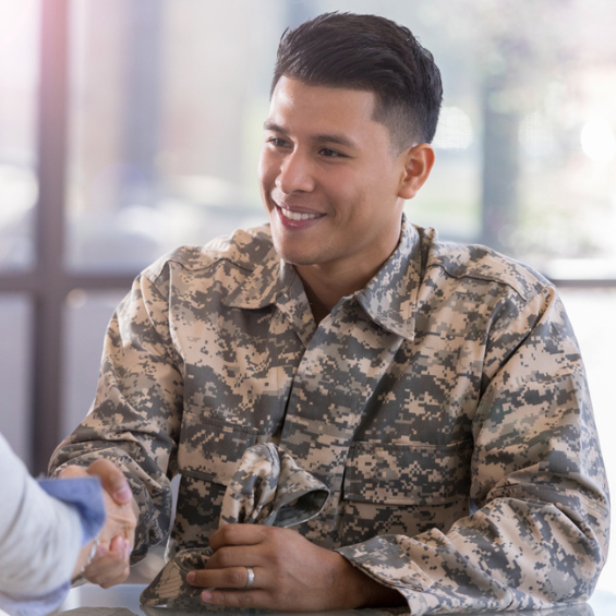 a man wearing camouflage fatigues and a wedding band shakes the hand of someone off camera