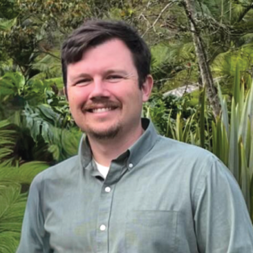 A white man with brown hair wearing a green shirt smiles at the camera