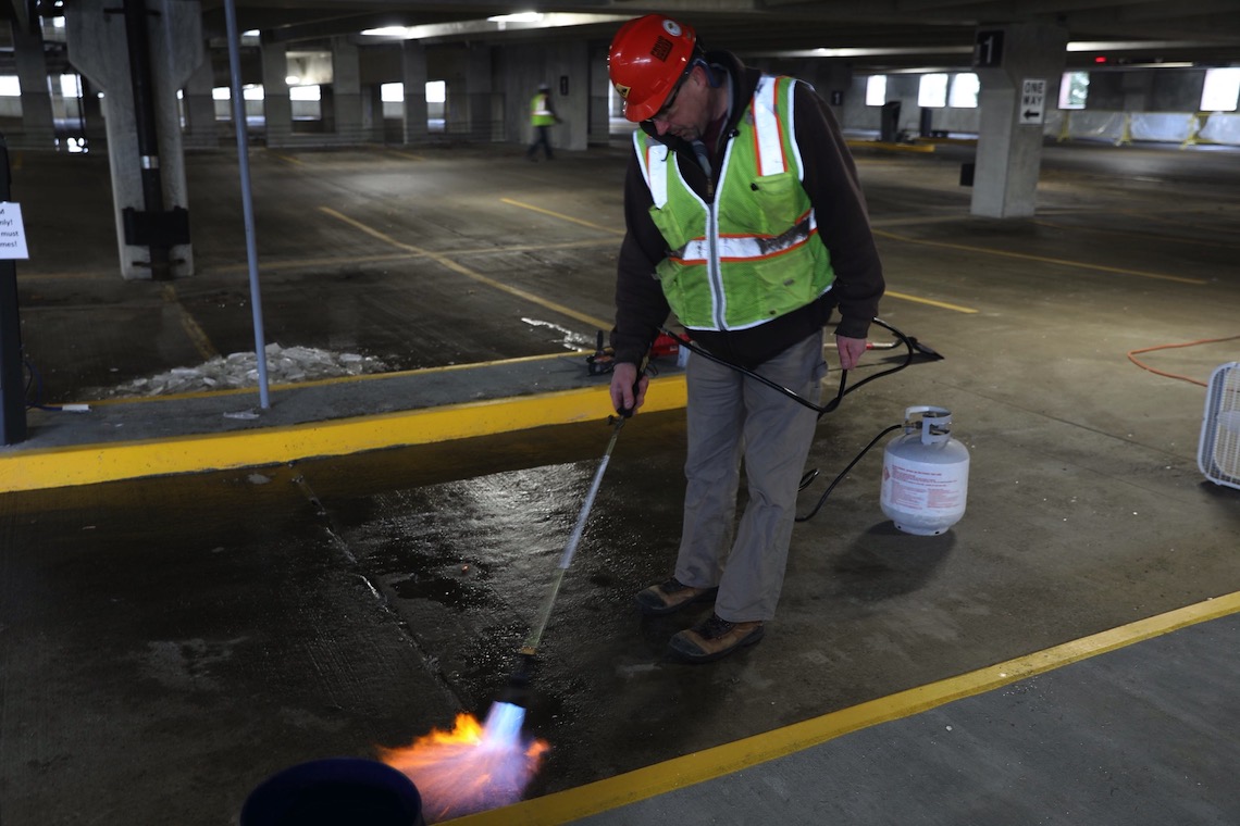A blowtorch dries out the pavement in the Portland parking garage before it can be painted with directional markings for the new traffic pattern.