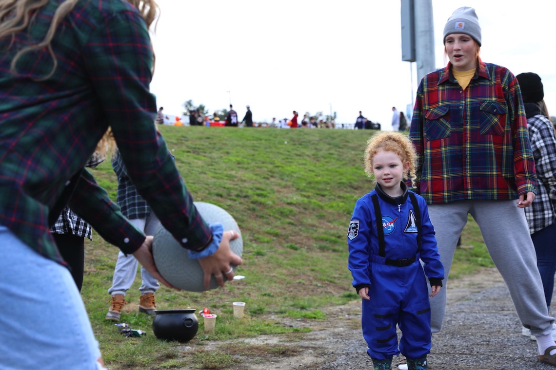 Student athletes coax a trick-or-treater dressed as an astronaut to play catch with them at the Husky Community Halloween Party.