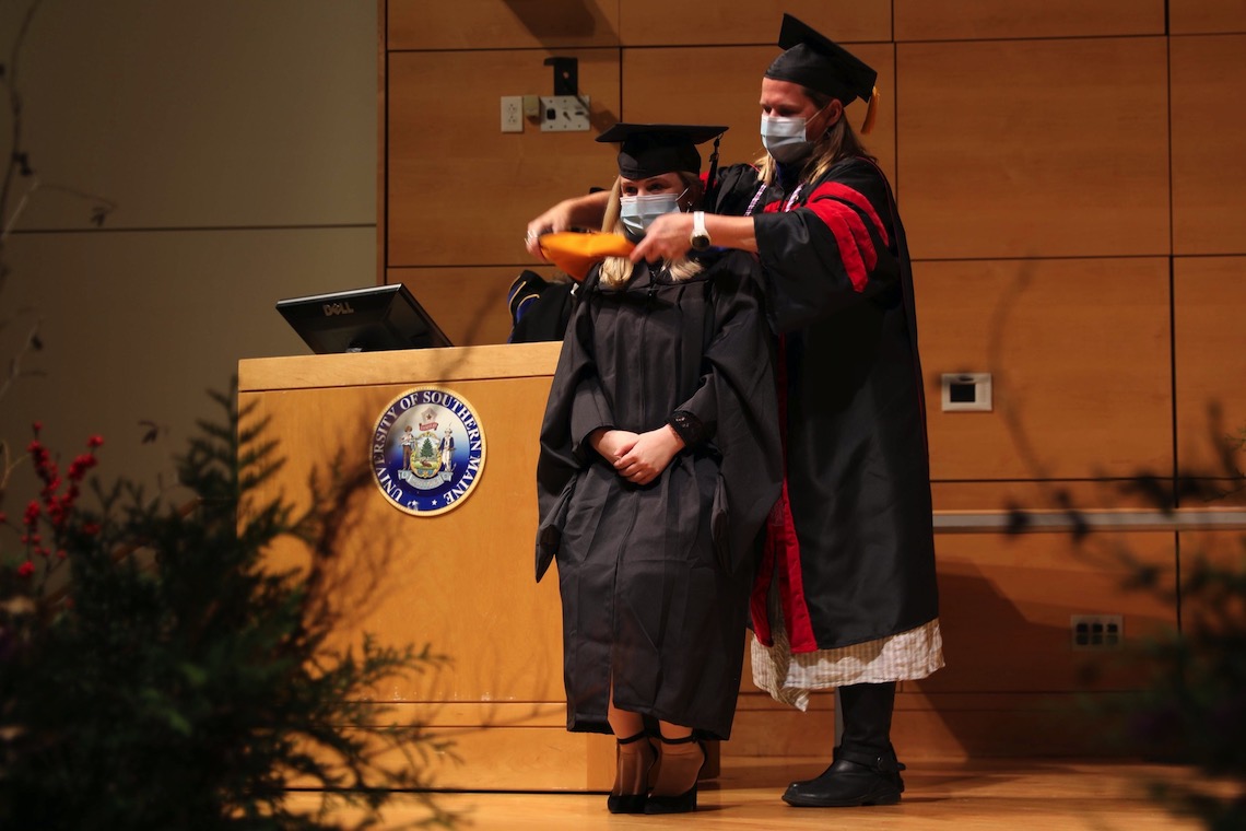 A master's-level graduate from the Nursing program stoops down to receive her traditional hood.