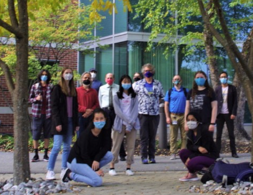 A group of masked students and faculty pose for a photo in front of the Science Building C-Wing entrance.