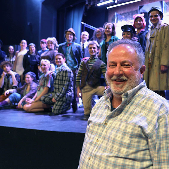 Ed Reichert standing in front of a stage with theatre students behind him.