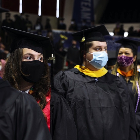Masked students wearing their graduation gowns wait in line to receive their diplomas.