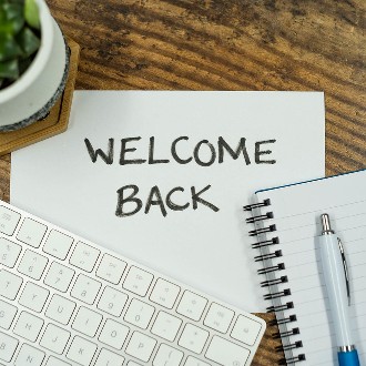 "Welcome Back" written on a sheet of paper above a keyboard, pen and notebook