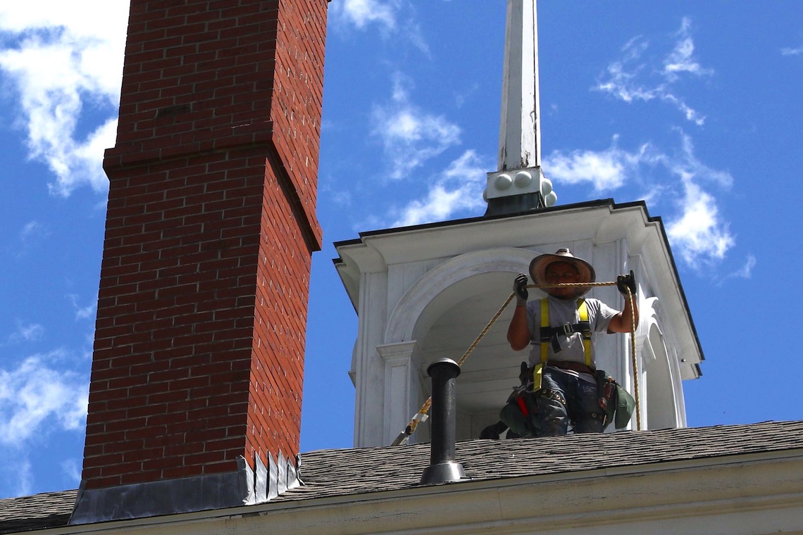 A roofer takes a break from laying new shingles on the Academy Building to check his equipment.