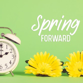 White alarm clock next to yellow daffodil flowers with the text "Spring Forward" above it.