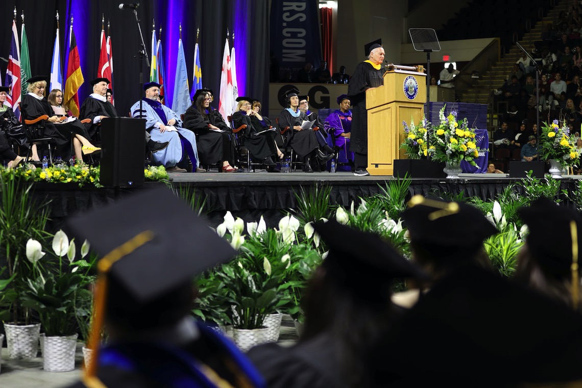 The stage part of distinguished faculty and guests listens to New York Times writer Neil Genzlinger as he delivers the keynote speech at the 2023 Commencement.