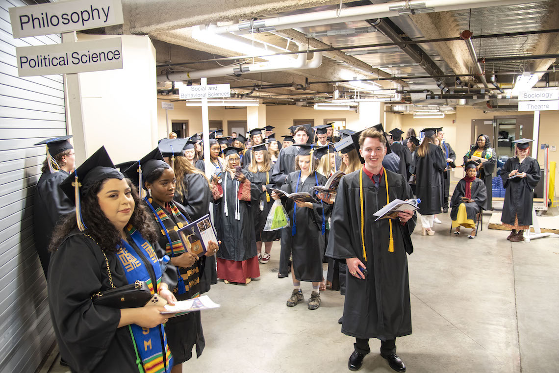 As the minutes tick away toward the start of the 2023 Commencement, graduates in the dressing area pass the time by chatting, checking their phones, and touching up their makeup.