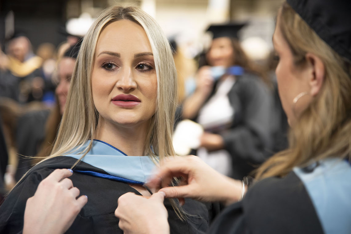 A student gets help adjusting her gown ahead of the 2023 Commencement.