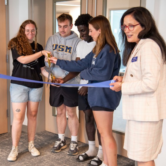 Students wield a pair of scissors while President Jacqueline Edmondson holds the ribbon at a ceremony to open the new Portland Commons complex.