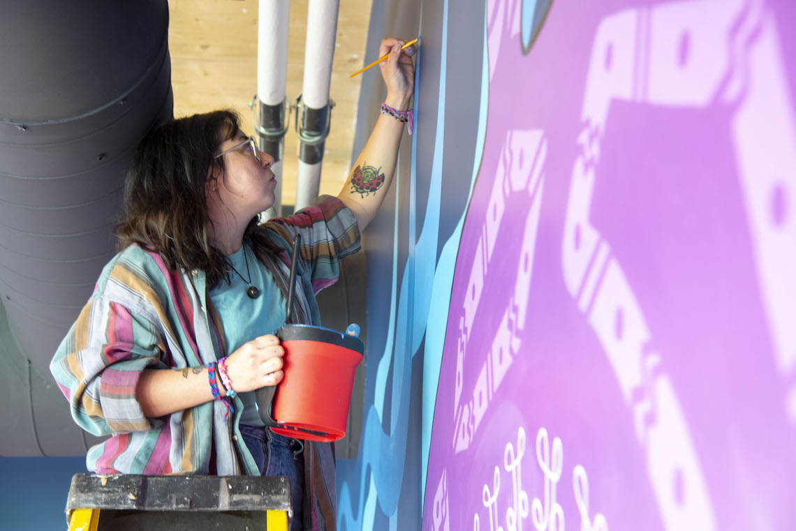 Marissa Joly worked around ventilation ducts and utility lines to complete the upper portions of her mural in the McGoldrick Center.