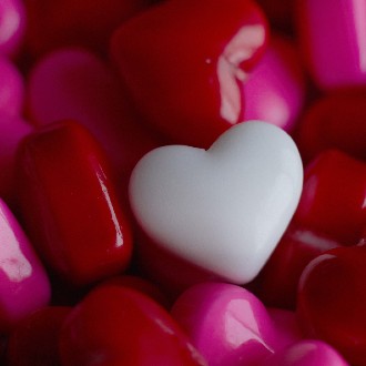 One white candy heart in the middle of a pile of red and pink hearts